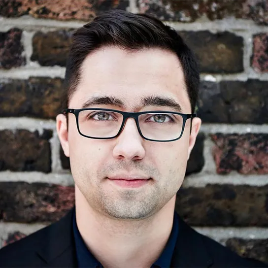 Team member Michael wearing glasses with a brick wall behind him