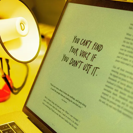Megaphone sits on a desk next to a macbook air displaying the words "You can't find your voice if you don't use it".