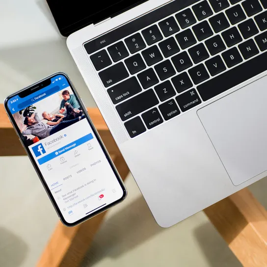 A laptop and mobile phone side by side, phone displays the social media platform facebook